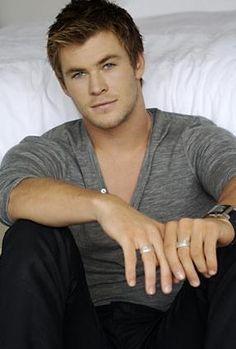 a young man sitting on top of a bed next to a white pillow in a bedroom