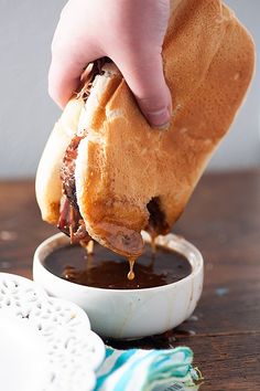 a person dipping sauce onto a sandwich in a bowl