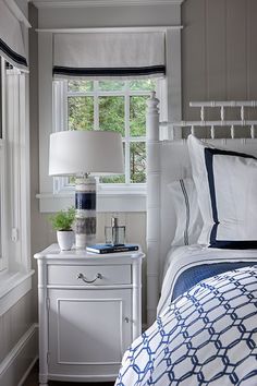 a bedroom with a bed, night stand and lamp in it's corner next to a window