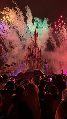 fireworks are lit up in the night sky above a castle with people holding umbrellas