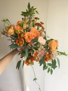 a bouquet of flowers is being held up by someone's hand in front of a white wall