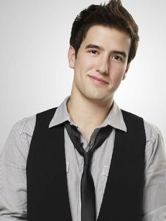 a young man wearing a black vest and tie posing for a photo with his arms crossed