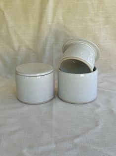 two white canisters sitting next to each other on a white cloth covered surface