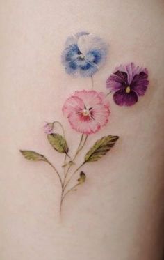 three colorful flowers on the side of a woman's thigh, with leaves and petals