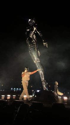 a man standing on top of a stage next to a giant skeleton statue at night