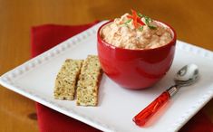 a red bowl filled with food sitting on top of a white plate next to crackers