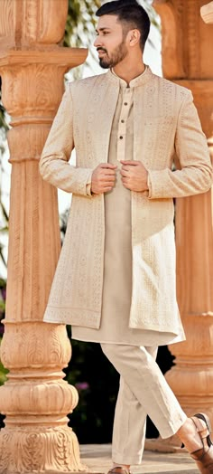 a man wearing a white sherwa with a beige jacket and pants on his feet