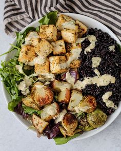 a white bowl filled with tahiti ranch tofu, vegetables and black rice on top