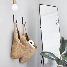 two bags hanging on the wall next to a mirror and toilet paper roll in a bag