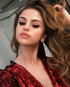 a woman with long brown hair wearing red sequins and silver earrings, standing in front of a mirror