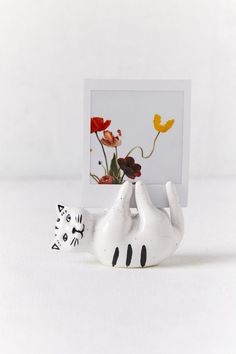 a white cat figurine sitting next to a photo frame with flowers on it