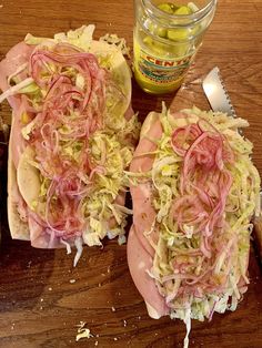 two ham sandwiches with coleslaw and pickles next to a jar of pickles