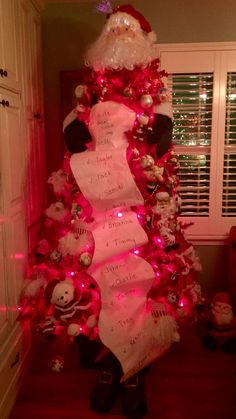 a decorated christmas tree with santa claus's hat on top and pink lights around it