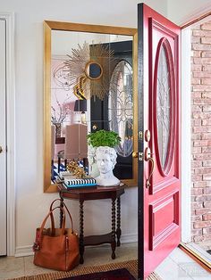 a red door is opened to reveal a mirror and purse on a table in front of it