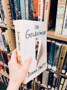 a person holding up a book in front of a bookshelf full of books