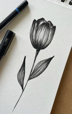 a black and white drawing of a flower on a piece of paper next to a pen