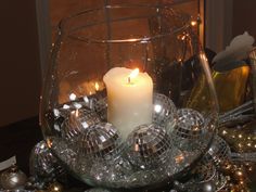 a candle is lit in a glass bowl with disco balls around it on a table