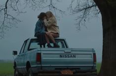 two people sitting on the back of a pick up truck in front of a tree