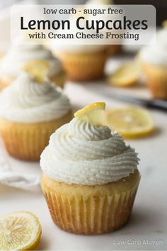 lemon cupcakes with cream cheese frosting on a white surface and sliced lemons in the background