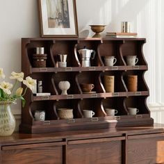 a wooden shelf filled with cups and saucers on top of a table next to a vase