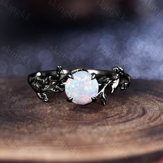 a white opal ring with leaves on it sitting on top of a piece of wood