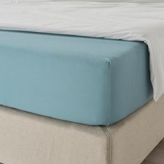 a close up view of a bed with a blue cover and white sheets on it