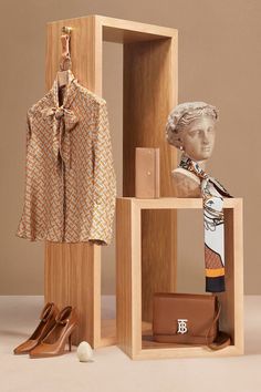 a wooden display case with shoes, purses and clothing on it in front of a mannequin's head