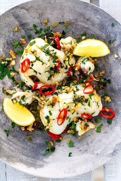 a plate filled with fish covered in sauce and garnished with herbs, next to a lemon wedge