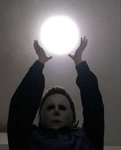 a person wearing a mask holds their hands up in the air with one hand above his head