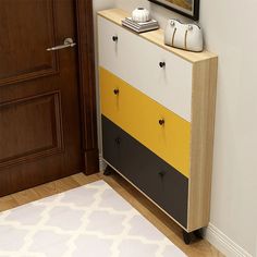 a white and yellow dresser next to a brown door with a painting on the wall