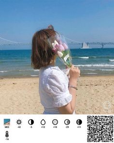 a girl on the beach with flowers in her hand and a bridge in the background