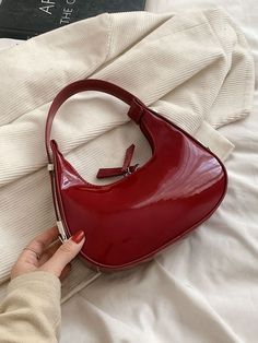 a woman's hand holding onto a red purse on top of a white bed