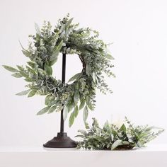 two wreaths sitting next to each other on top of a white table with candles