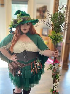 a woman dressed in green and white holding a stick with plants on it's sides