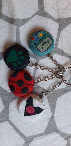 three ladybug key chains are sitting on top of a white sheet with black and red designs