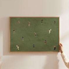 a person is holding up a painting with people playing soccer on it in the room