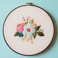 an embroidered flower is shown on a white hoop with blue and pink flowers in the center