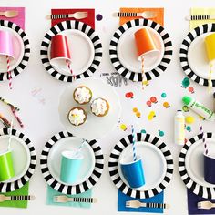 the table is set with colorful plates, cups and utensils for desserts