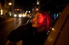 a woman with red hair sitting in the back seat of a car on a city street at night