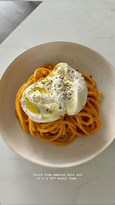 a white bowl filled with pasta and topped with an egg on top, sitting on a marble countertop