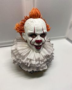 a close up of a creepy clown mask on a white surface with an orange hair