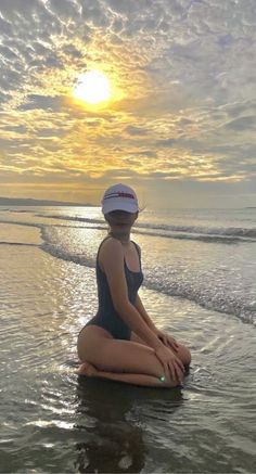 a woman sitting in the water on top of a surfboard near the ocean at sunset