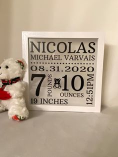 a white teddy bear sitting next to a birth announcement sign on a table with a red heart