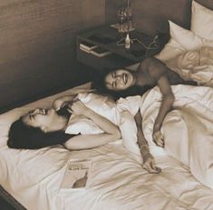 two women laying on a bed with white sheets