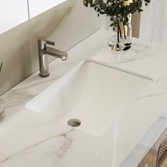 a white bathroom sink sitting next to a counter with flowers in vases on it