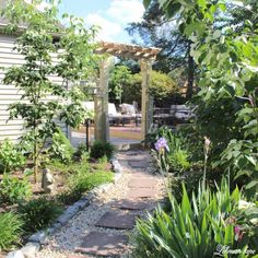 a garden with rocks and plants in the foreground, an outdoor patio on the far side