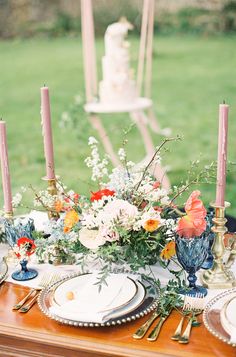 the table is set with flowers and candles for an outdoor wedding reception in front of a grassy field