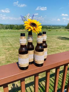 three brown bottles with sunflowers in them sitting on a deck