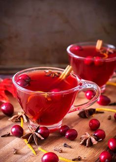 two glasses of cranberry tea on a wooden table with cinnamon sticks in them