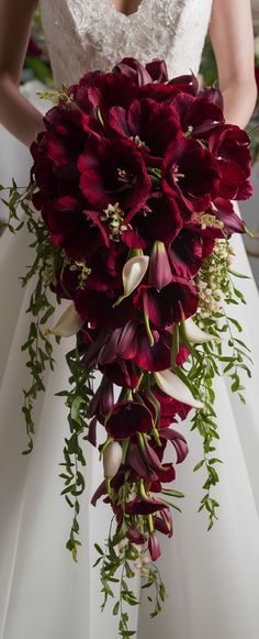 a bride holding a bouquet of red flowers and greenery on her wedding day,